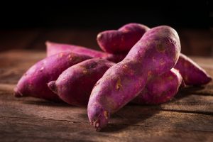 Close-up of purple sweet potatoes on a wooden surface, perfect for culinary and natural food themes.
