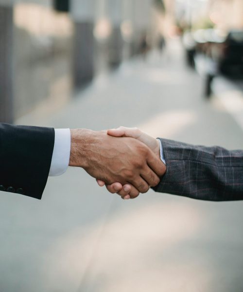Two businessmen shaking hands outside, symbolizing cooperation and agreement in a city setting.